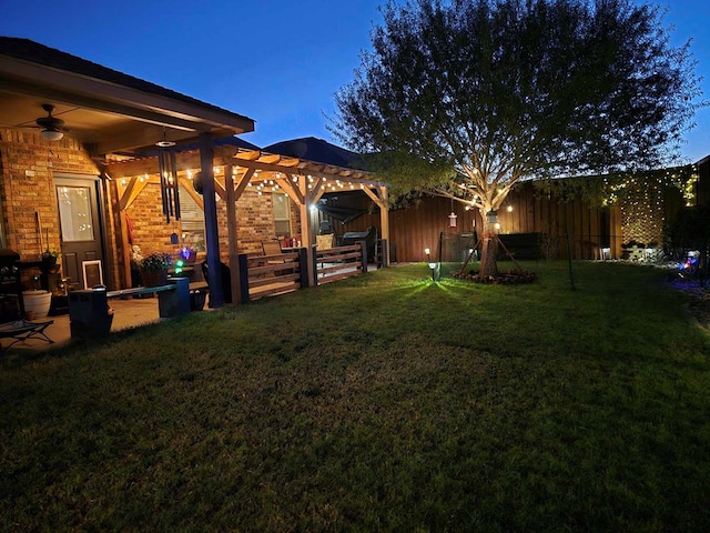 yard at dusk featuring ceiling fan and a pergola