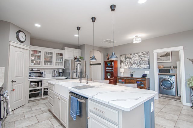 kitchen with washer / dryer, decorative light fixtures, white cabinetry, stainless steel appliances, and an island with sink