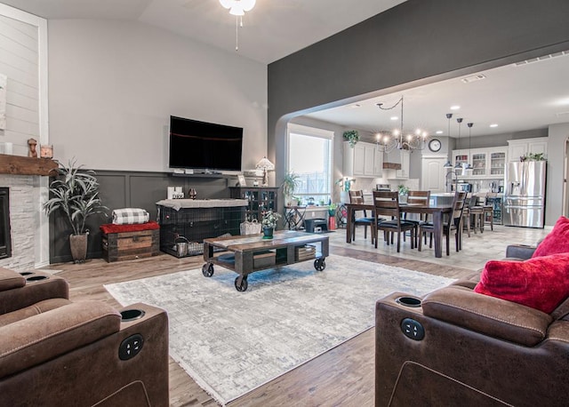 living room featuring lofted ceiling, ceiling fan with notable chandelier, a stone fireplace, and light hardwood / wood-style floors