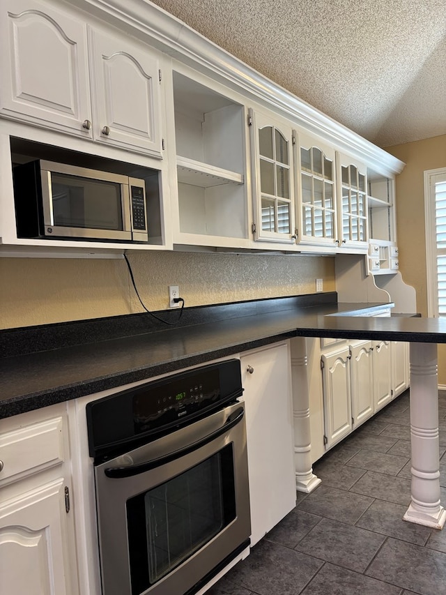 3507 Edgemont Dr, Midland, TX 79707 - kitchen featuring appliances with stainless steel finishes, dark countertops, open shelves, a textured ceiling, and white cabinetry