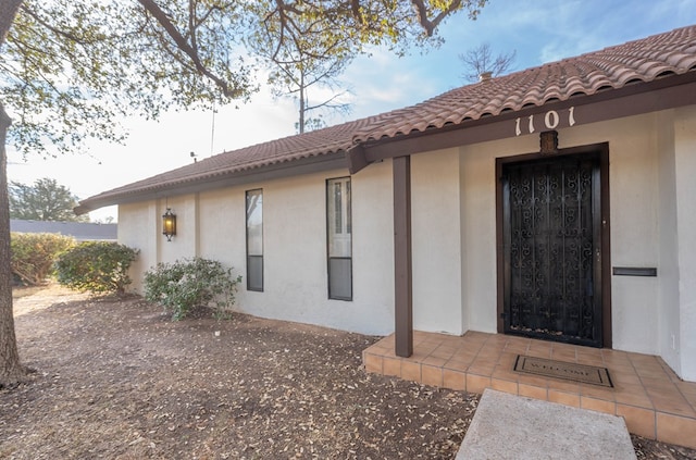 view of exterior entry featuring a tiled roof and stucco siding