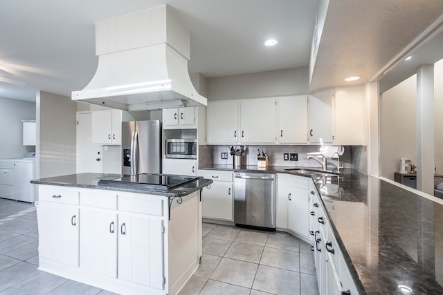 kitchen with stainless steel appliances, washing machine and dryer, white cabinets, a sink, and premium range hood