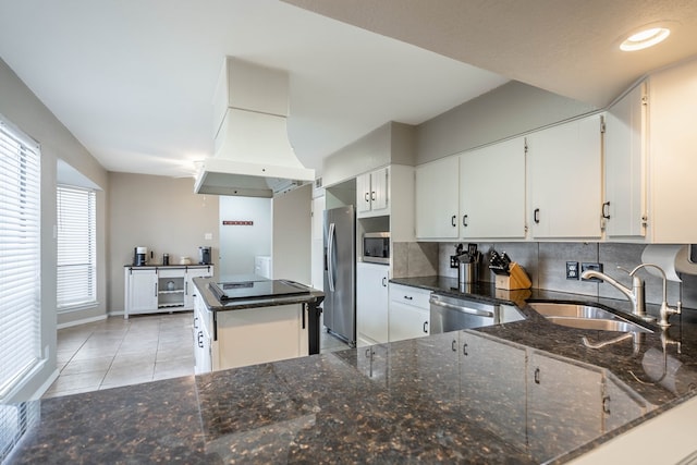 kitchen featuring tasteful backsplash, dark stone counters, appliances with stainless steel finishes, island exhaust hood, and a sink