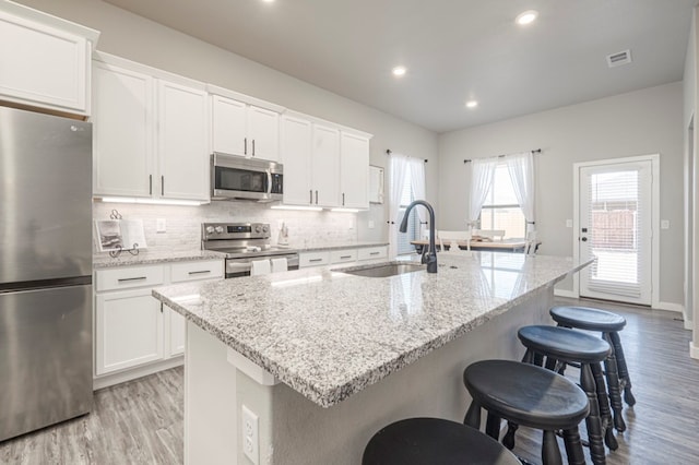 kitchen with white cabinetry, appliances with stainless steel finishes, sink, and a kitchen island with sink