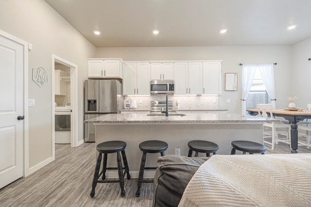 kitchen with appliances with stainless steel finishes, light stone countertops, white cabinets, a center island with sink, and washer / clothes dryer