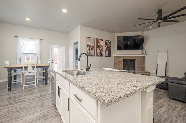 kitchen featuring white cabinetry, an island with sink, sink, light stone counters, and light hardwood / wood-style flooring