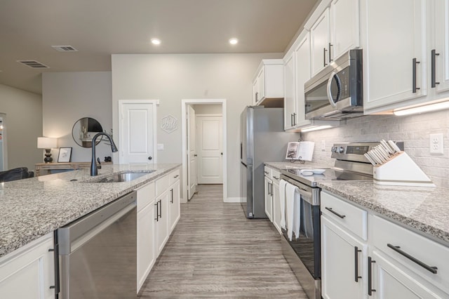 kitchen with sink, stainless steel appliances, light stone counters, tasteful backsplash, and white cabinets