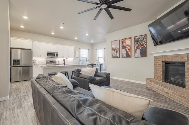 living room featuring lofted ceiling, a fireplace, light hardwood / wood-style floors, and ceiling fan