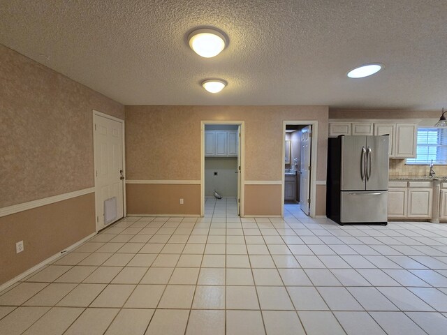 4908 Timber Ct, Midland, TX 79707 - kitchen with freestanding refrigerator, a textured ceiling, light tile patterned floors, white cabinets, and baseboards
