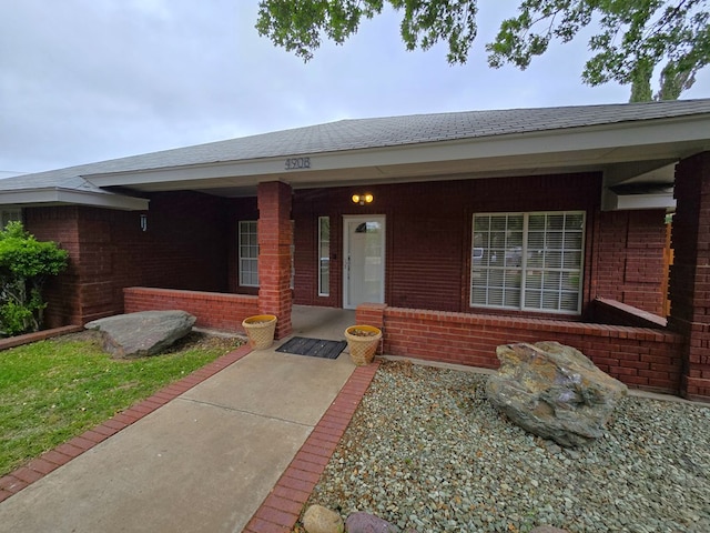 4908 Timber Ct, Midland, TX 79707 - doorway to property featuring a porch, brick siding, and a shingled roof