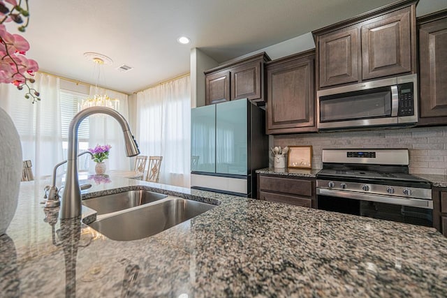 7009 Mcpherson Ln, Midland, TX 79706 - kitchen featuring appliances with stainless steel finishes, a sink, a chandelier, dark brown cabinetry, and dark stone counters
