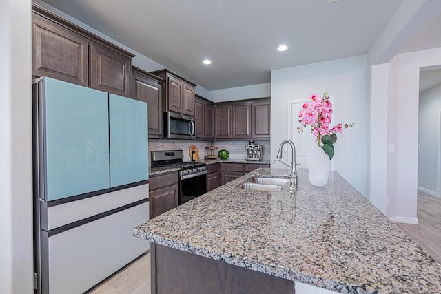 7009 Mcpherson Ln, Midland, TX 79706 - kitchen featuring stainless steel appliances, a sink, dark brown cabinetry, light stone countertops, and light wood-style floors