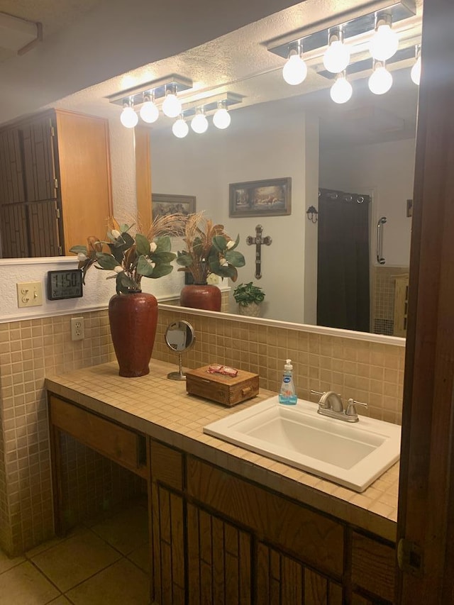 bathroom with a textured ceiling, vanity, tile walls, wainscoting, and tile patterned floors