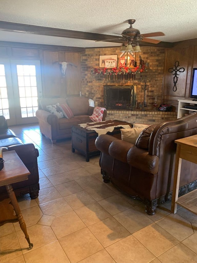 living room with a brick fireplace, light tile patterned flooring, ceiling fan, and a textured ceiling