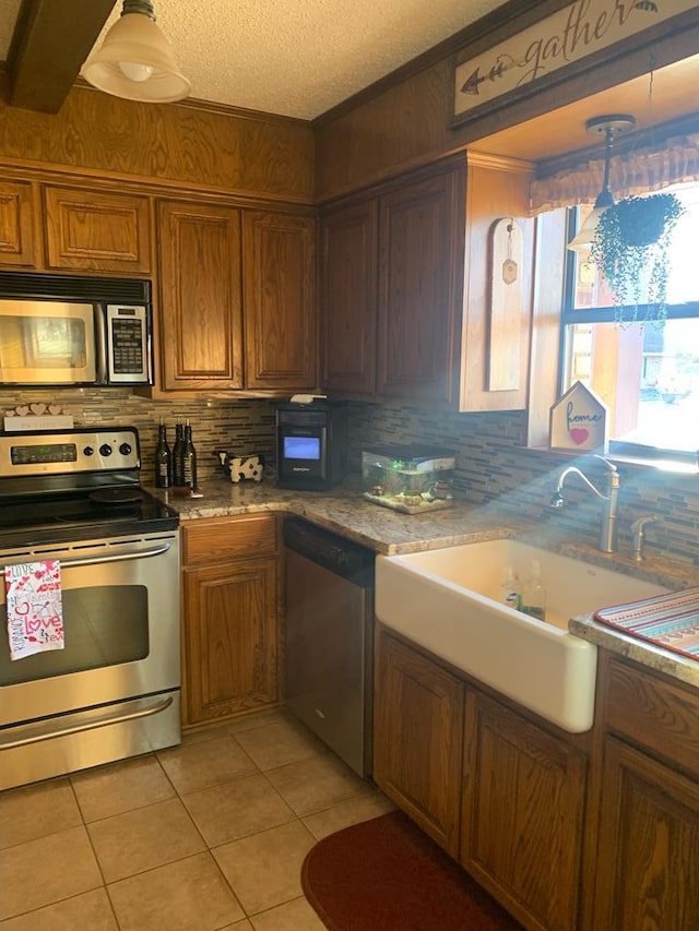 kitchen with light tile patterned floors, a textured ceiling, a sink, appliances with stainless steel finishes, and brown cabinets