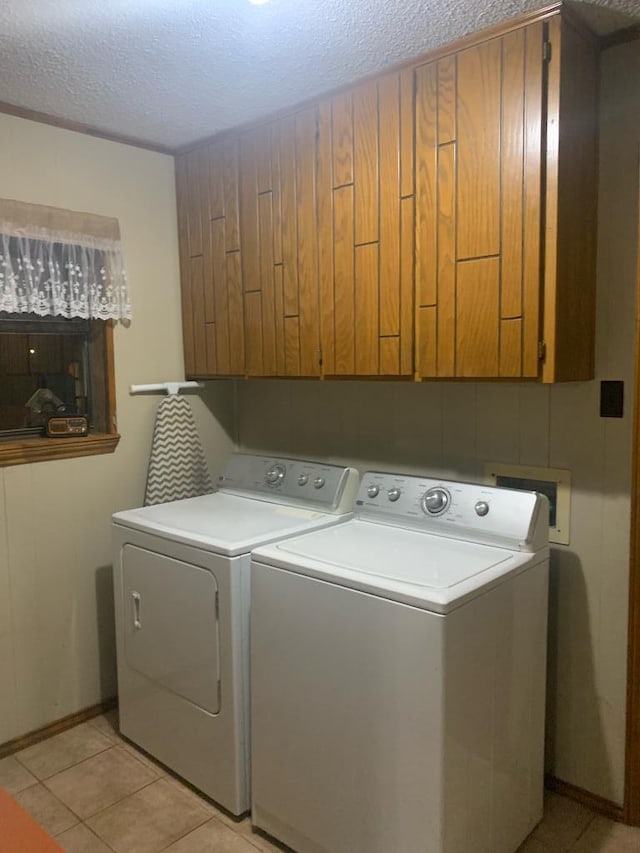 clothes washing area featuring washing machine and dryer, cabinet space, a textured ceiling, and light tile patterned flooring