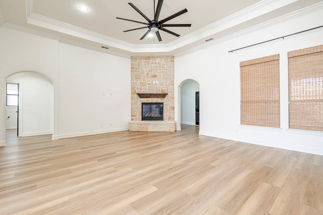 unfurnished living room with a raised ceiling, ceiling fan, a stone fireplace, and crown molding