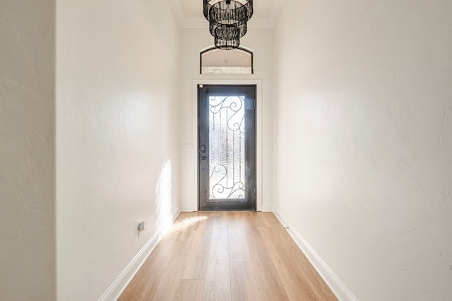 doorway with light hardwood / wood-style flooring, an inviting chandelier, and ornamental molding