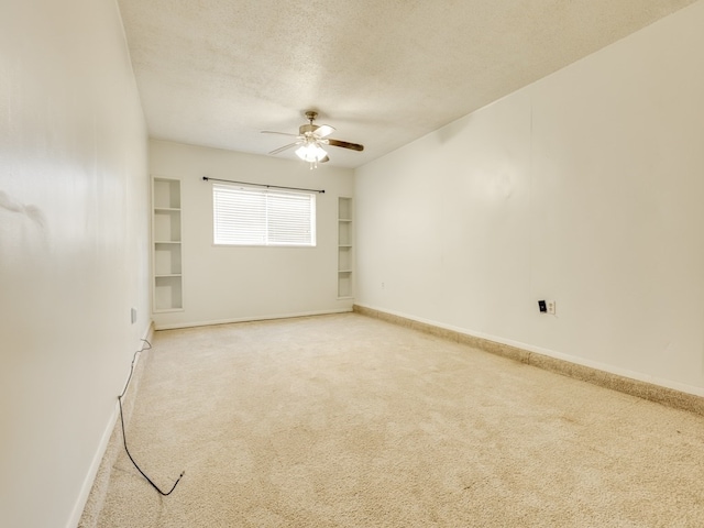 carpeted spare room with ceiling fan, a textured ceiling, and built in shelves