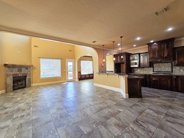 kitchen with stainless steel microwave, a kitchen breakfast bar, backsplash, decorative light fixtures, and a fireplace