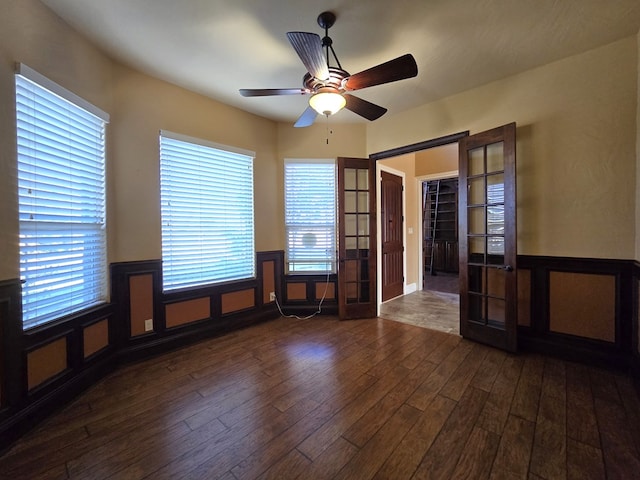 spare room featuring french doors, ceiling fan, a wainscoted wall, and dark wood-style floors