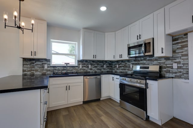 kitchen with appliances with stainless steel finishes, a sink, dark countertops, dark wood-type flooring, and white cabinets