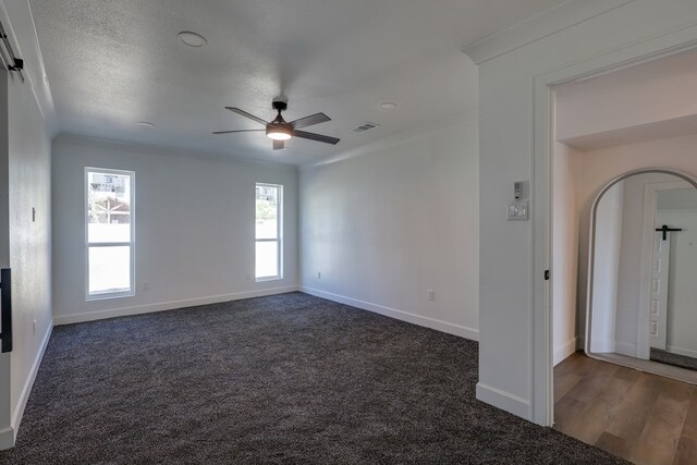empty room with ornamental molding, a ceiling fan, baseboards, arched walkways, and carpet floors