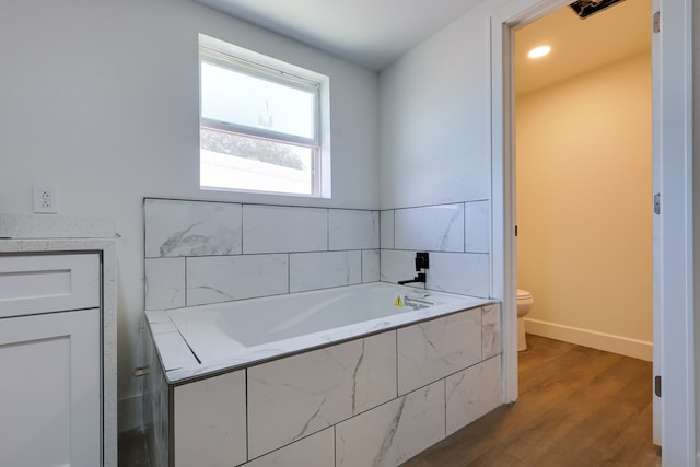 bathroom with toilet, a garden tub, wood finished floors, baseboards, and vanity
