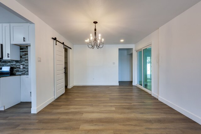 unfurnished dining area featuring a barn door, baseboards, wood finished floors, recessed lighting, and a chandelier
