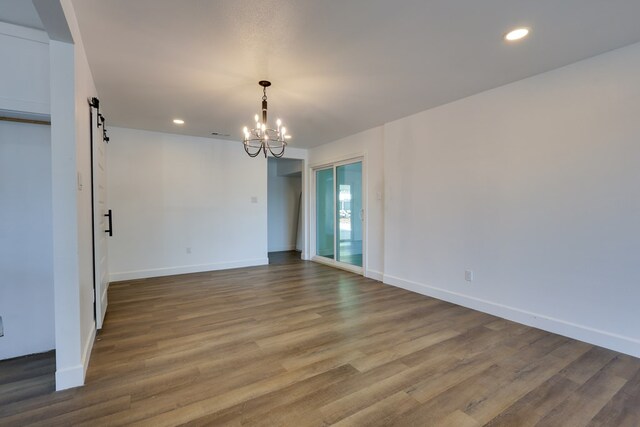unfurnished room with a barn door, a chandelier, baseboards, recessed lighting, and wood finished floors