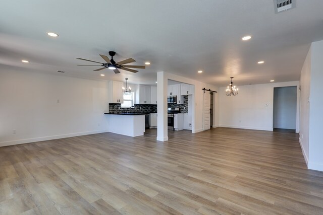 unfurnished living room with a chandelier, recessed lighting, a barn door, ceiling fan, and baseboards