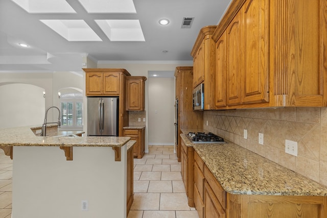 4906 Crista Ln, Midland, TX 79707 - kitchen with stainless steel appliances, a breakfast bar, arched walkways, brown cabinetry, and light stone countertops