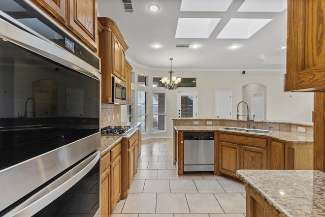 4906 Crista Ln, Midland, TX 79707 - kitchen featuring appliances with stainless steel finishes, a skylight, crown molding, brown cabinetry, and a chandelier
