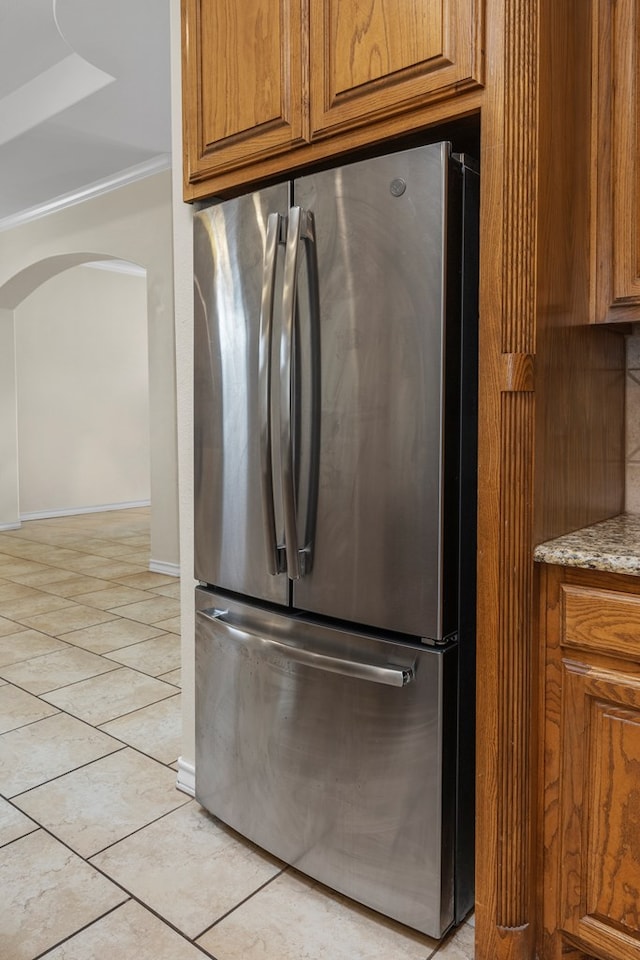 4906 Crista Ln, Midland, TX 79707 - kitchen view of freestanding refrigerator, brown cabinets, arched walkways, and light stone countertops