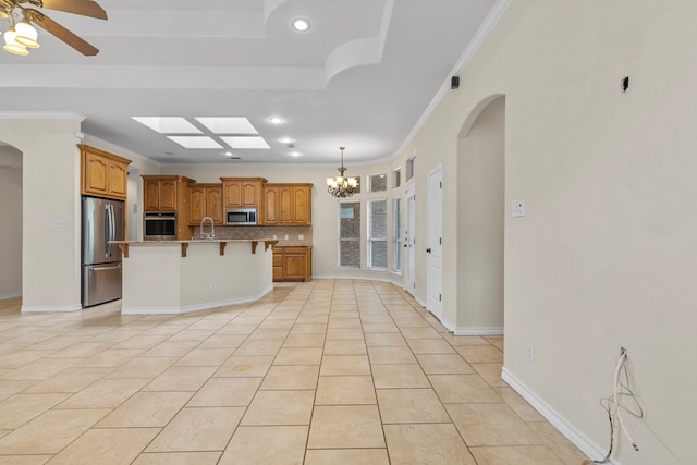 4906 Crista Ln, Midland, TX 79707 - kitchen featuring appliances with stainless steel finishes, arched walkways, a kitchen breakfast bar, brown cabinetry, and ornamental molding