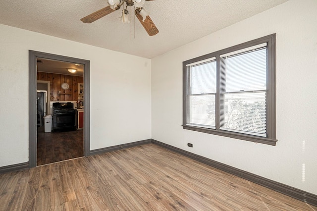 empty room with a ceiling fan, wood finished floors, baseboards, and a textured ceiling