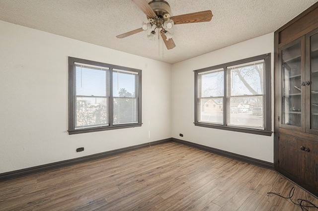 empty room featuring a textured ceiling, a ceiling fan, baseboards, and wood finished floors