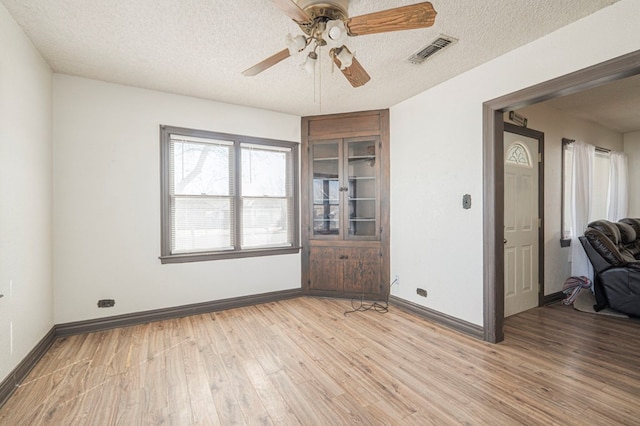 spare room with visible vents, baseboards, ceiling fan, light wood-style floors, and a textured ceiling