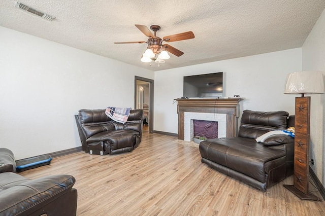 living room featuring a ceiling fan, visible vents, light wood-style flooring, a fireplace with flush hearth, and a textured ceiling