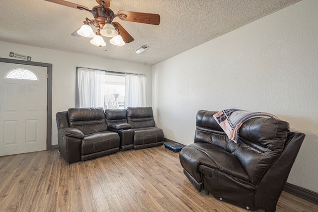 living area featuring visible vents, a textured ceiling, a ceiling fan, and light wood finished floors