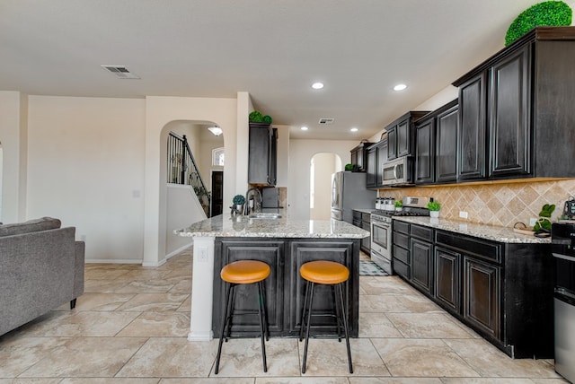 kitchen with arched walkways, decorative backsplash, appliances with stainless steel finishes, a breakfast bar area, and light stone countertops