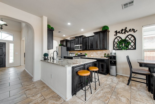 kitchen with arched walkways, dark cabinets, stainless steel appliances, visible vents, and a kitchen bar