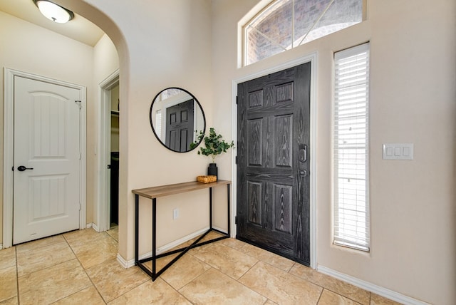 entryway with arched walkways, light tile patterned flooring, and baseboards