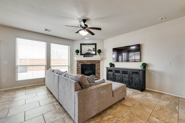 living area with ceiling fan, a stone fireplace, visible vents, and baseboards