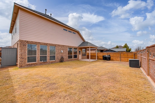 rear view of property featuring a fenced backyard, a lawn, a patio, and brick siding