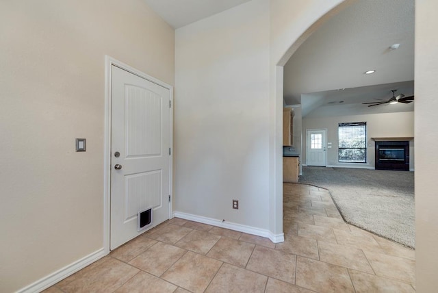spare room with arched walkways, a glass covered fireplace, baseboards, ceiling fan, and light colored carpet