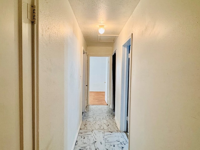 corridor featuring baseboards, attic access, marble finish floor, and a textured ceiling