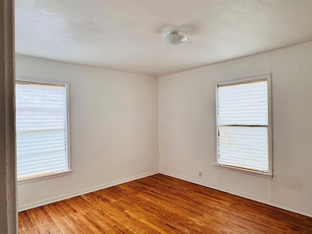 spare room with baseboards, wood finished floors, and a wealth of natural light