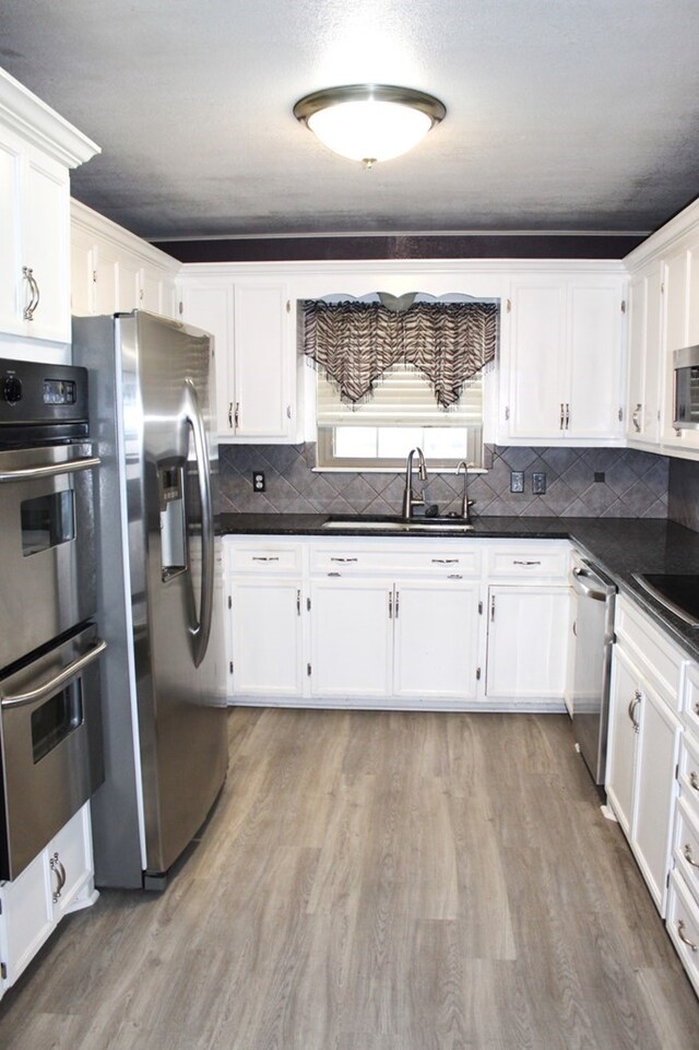 kitchen with sink, white cabinetry, stainless steel appliances, and light hardwood / wood-style flooring