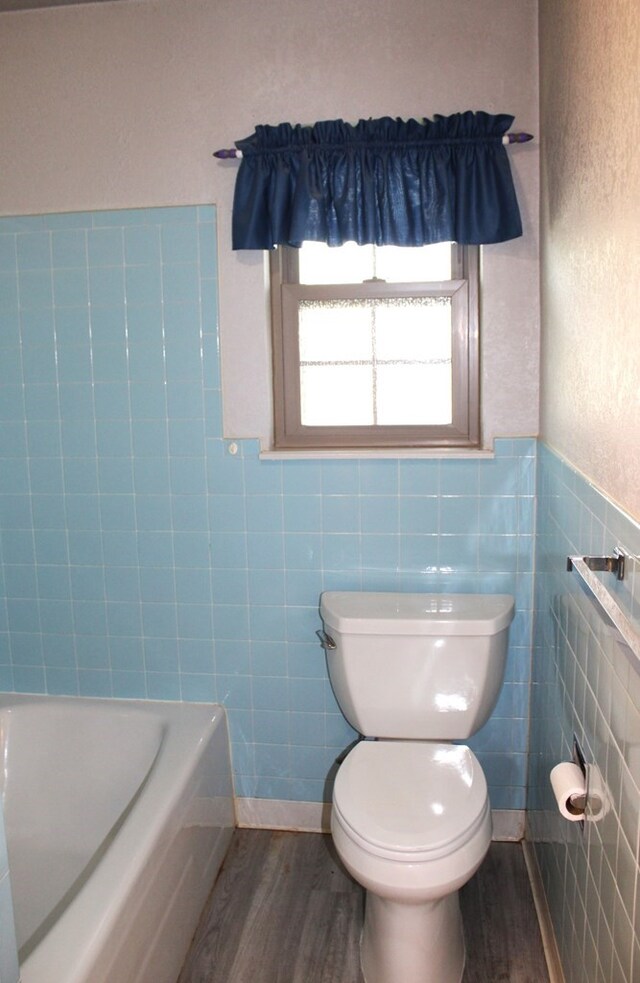 bathroom with hardwood / wood-style flooring, a bathtub, toilet, and tile walls